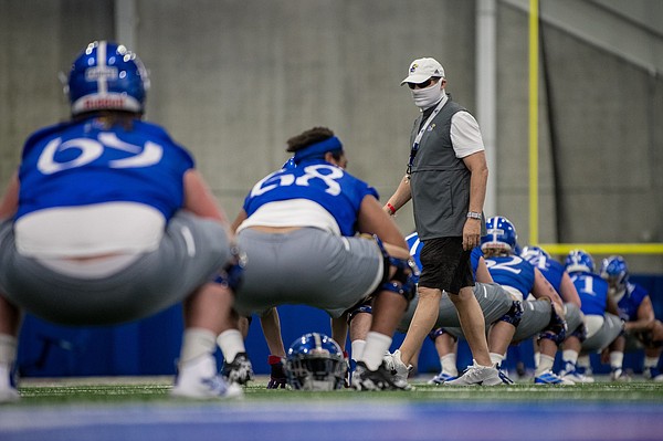 Kansas football head coach Les Miles wears a mask while walking around during an early August practice in the team's indoor facility.