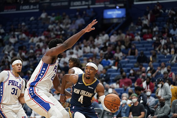 New Orleans Pelicans guard Devonte' Graham (4) passes around Philadelphia 76ers center Joel Embiid in the second half of an NBA basketball game in New Orleans, Wednesday, Oct. 20, 2021. The 76ers won 117-97. 