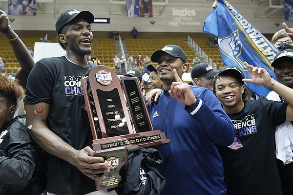 Chattanooga forward Silvio De Sousa, left, and head coach Lamont Paris hold the championship trophy to celebrate their win over Furman in an NCAA college basketball championship game for the Southern Conference tournament, Monday, March 7, 2022, in Asheville, N.C. (AP Photo/Kathy Kmonicek)
